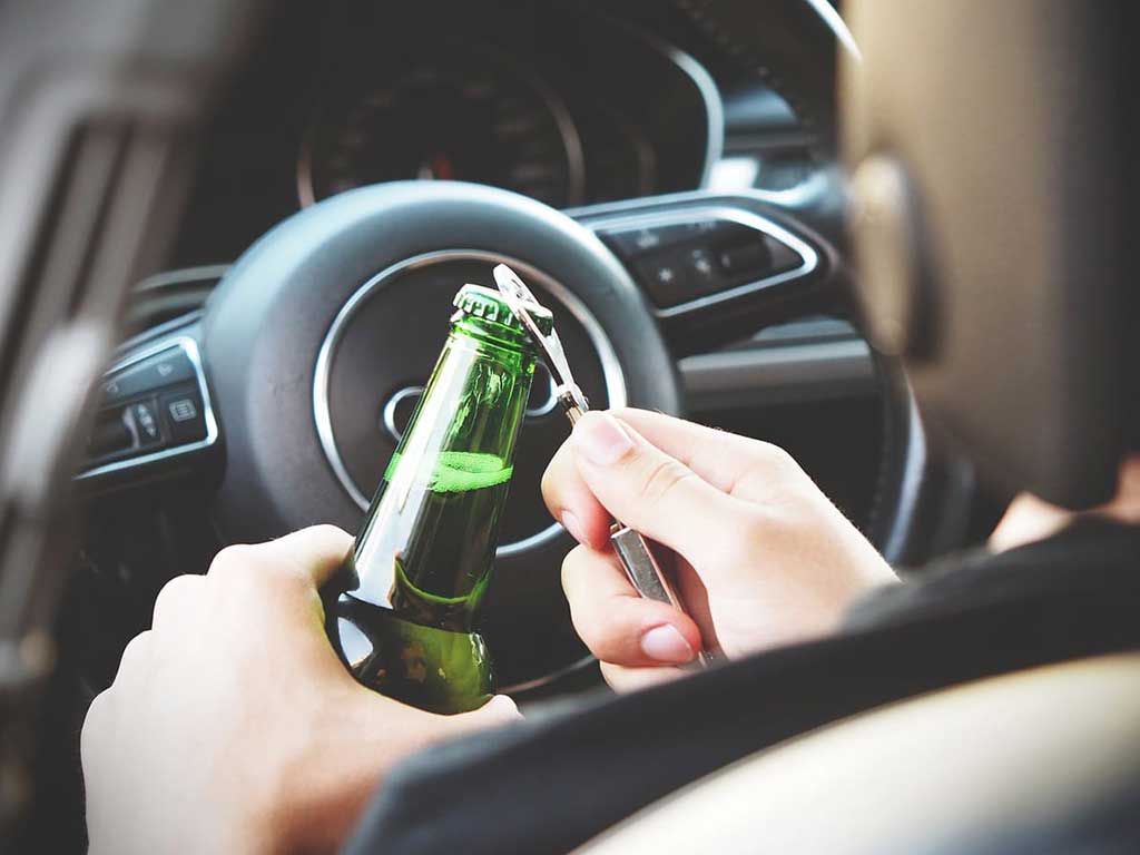 A person opening a bottle of beer inside the car.