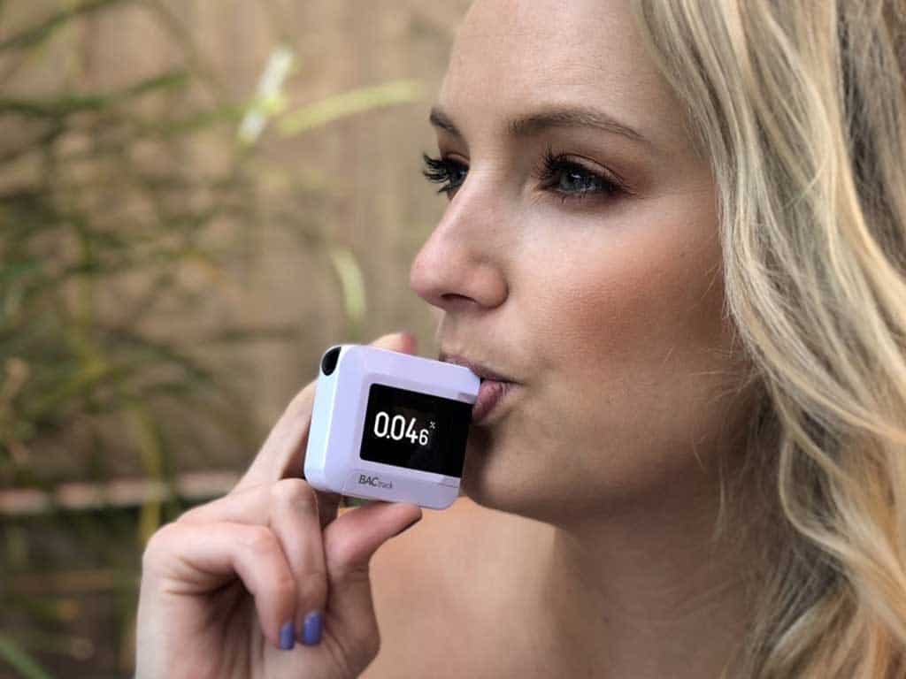 A woman conducting a breath test using a personal breathalyzer
