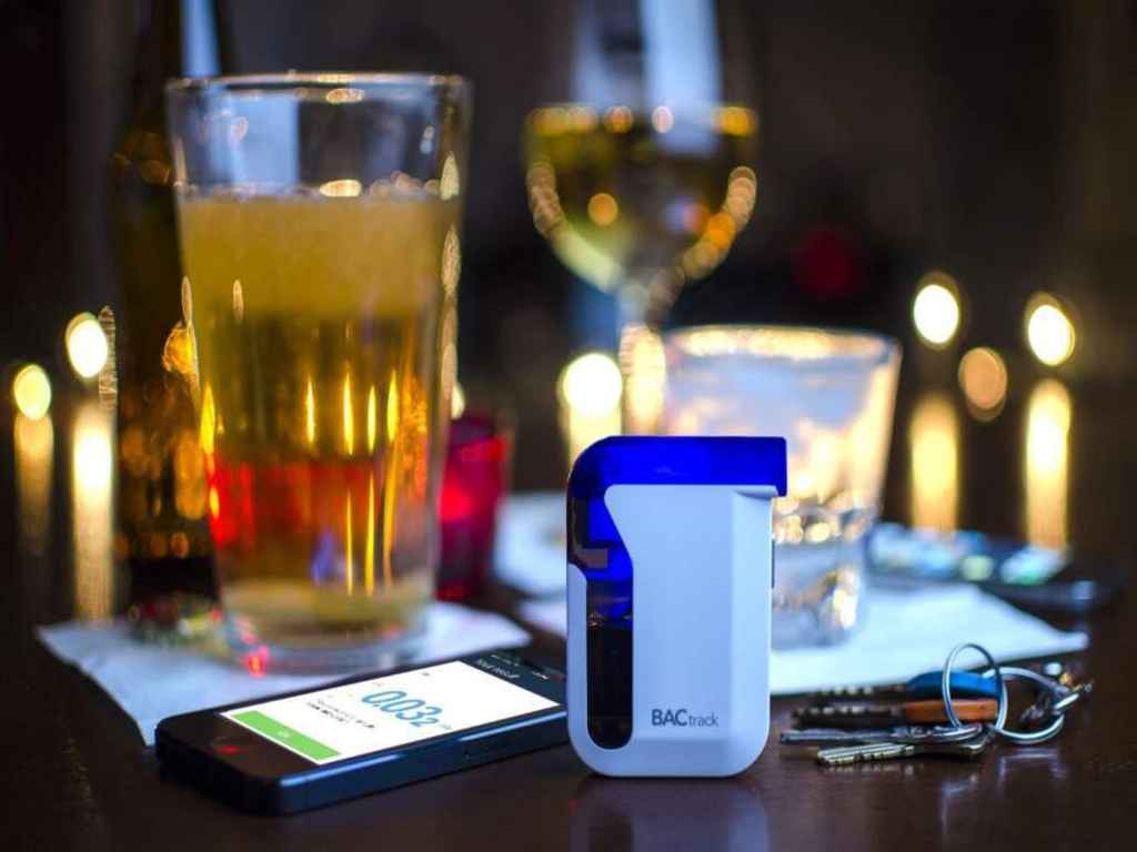 A breathalyser, a smartphone, and glasses of liquor on the table.