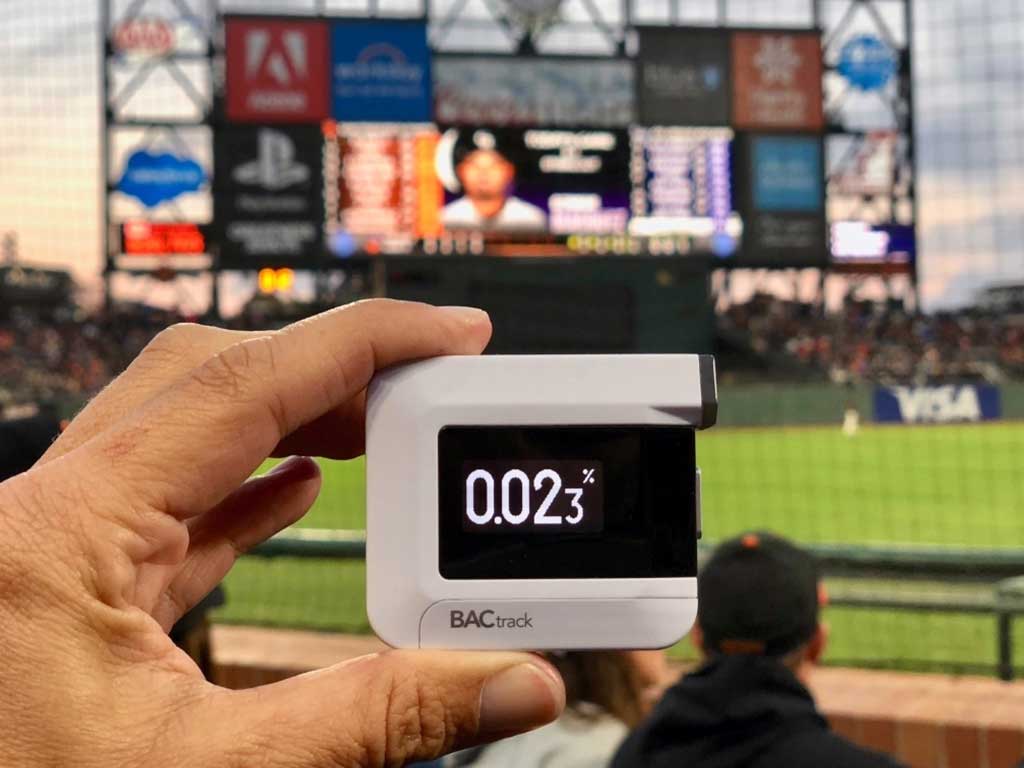 A person holding a breathalyzer at a baseball field