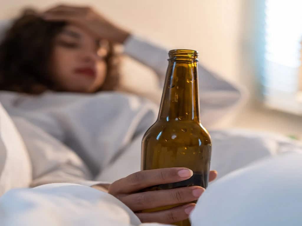 A woman on bed while she is holding a bottle of alcohol