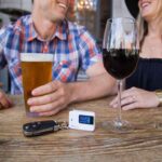 A man and a woman with alcoholic drinks, a key, and breathalyser on top of a table