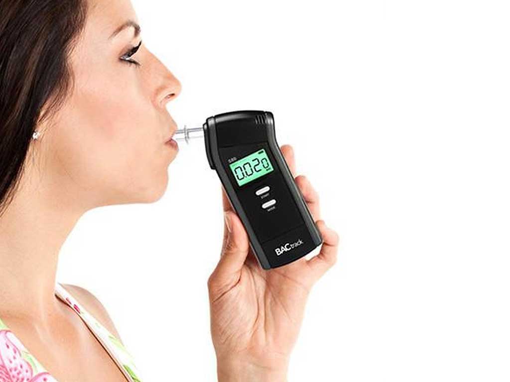 A woman blowing into a breathalyzer while it shows the result
