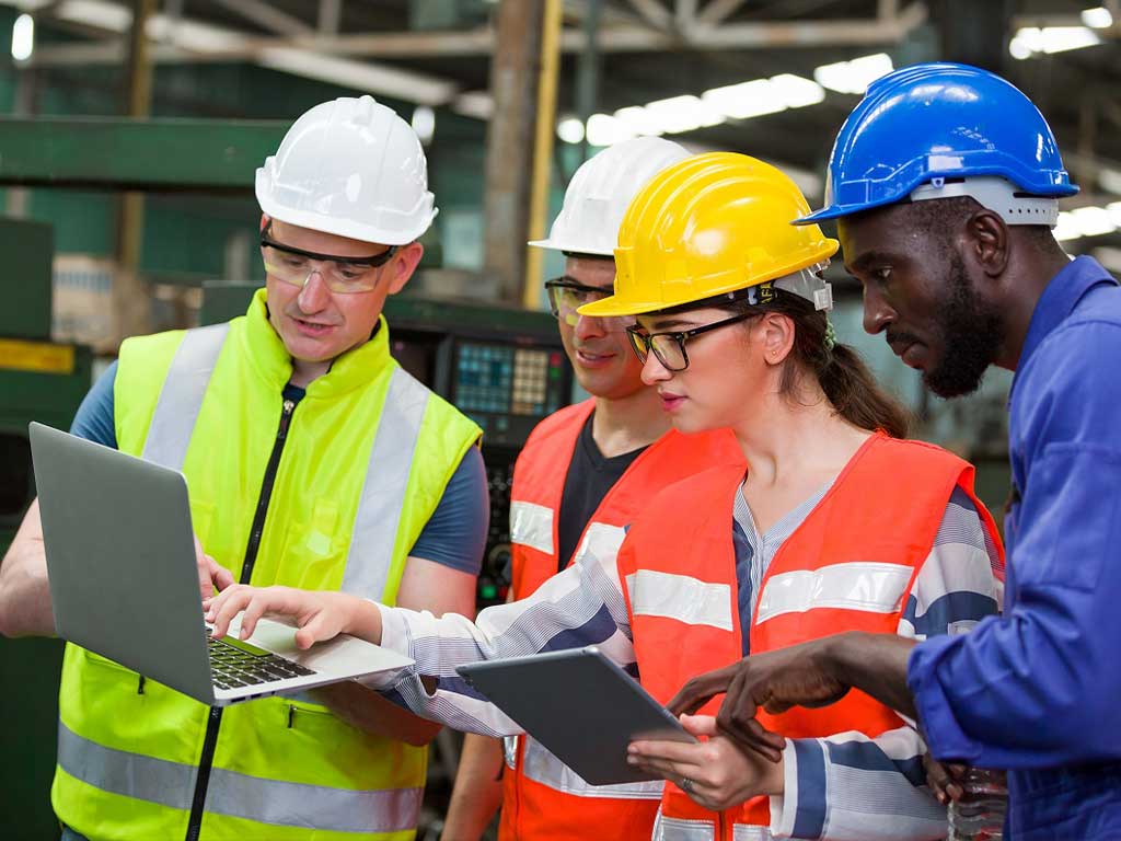 A group of workers wearing protective equipment looking at a laptop