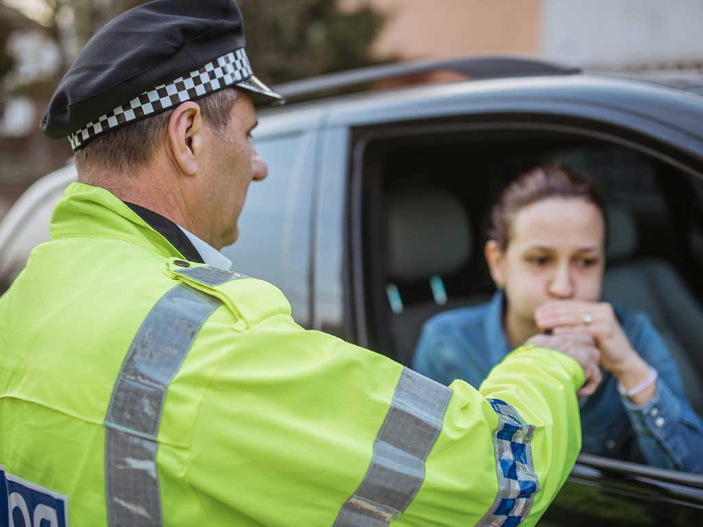 A police officer conducting a roadside breath test on a woman inside a car