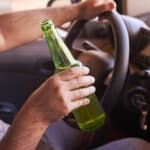 A person holding a bottle of alcohol while driving