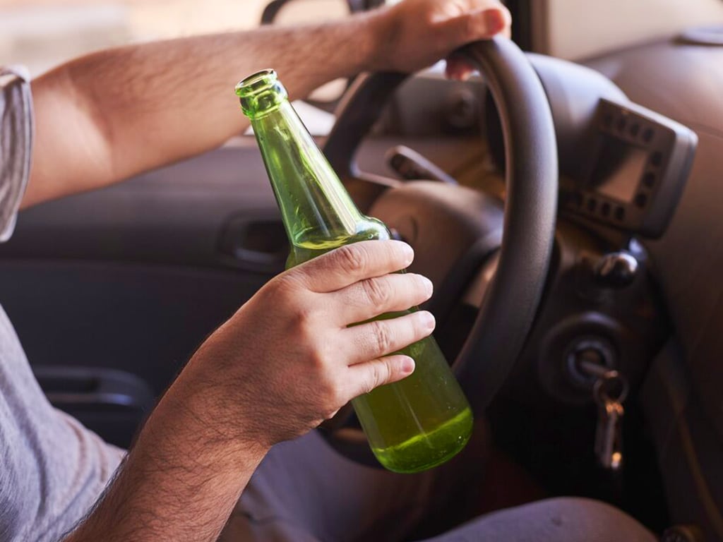 A person holding a bottle of alcohol while driving