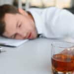 A staff member under the influence, slumbering on the table while clutching a glass of alcoholic beverage